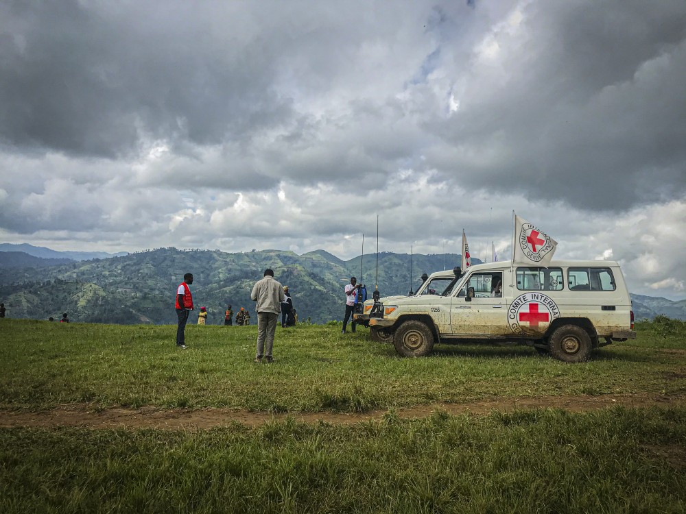 A group of people standing on a hill next to a red cross vehicle, publishing carbon footprints.