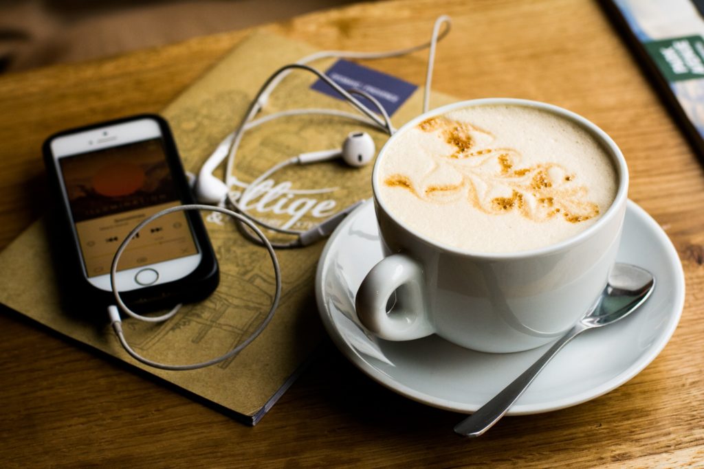 Une tasse de café avec des écouteurs à côté, prête pour notre podcast.