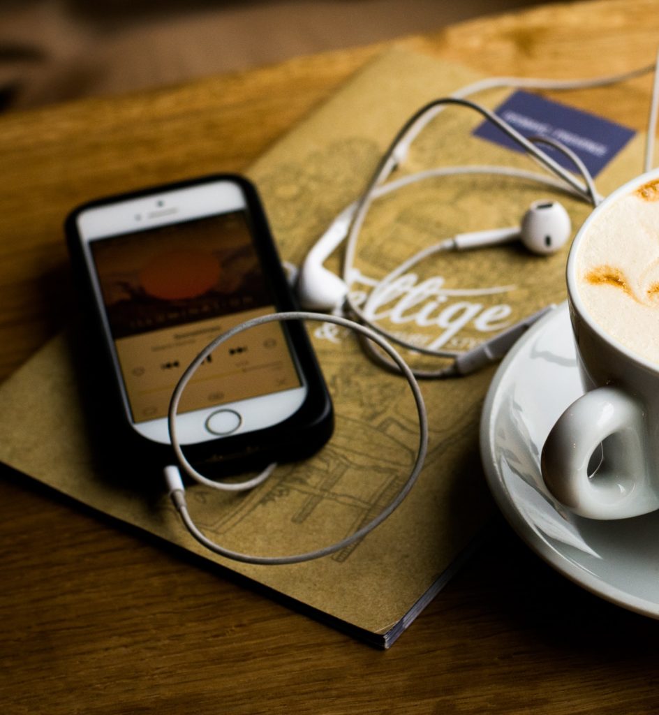 A cup of coffee with earphones next to it, perfect for enjoying our podcast.