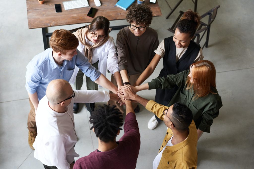 A group of people forming a circle, putting their hands together in unity.