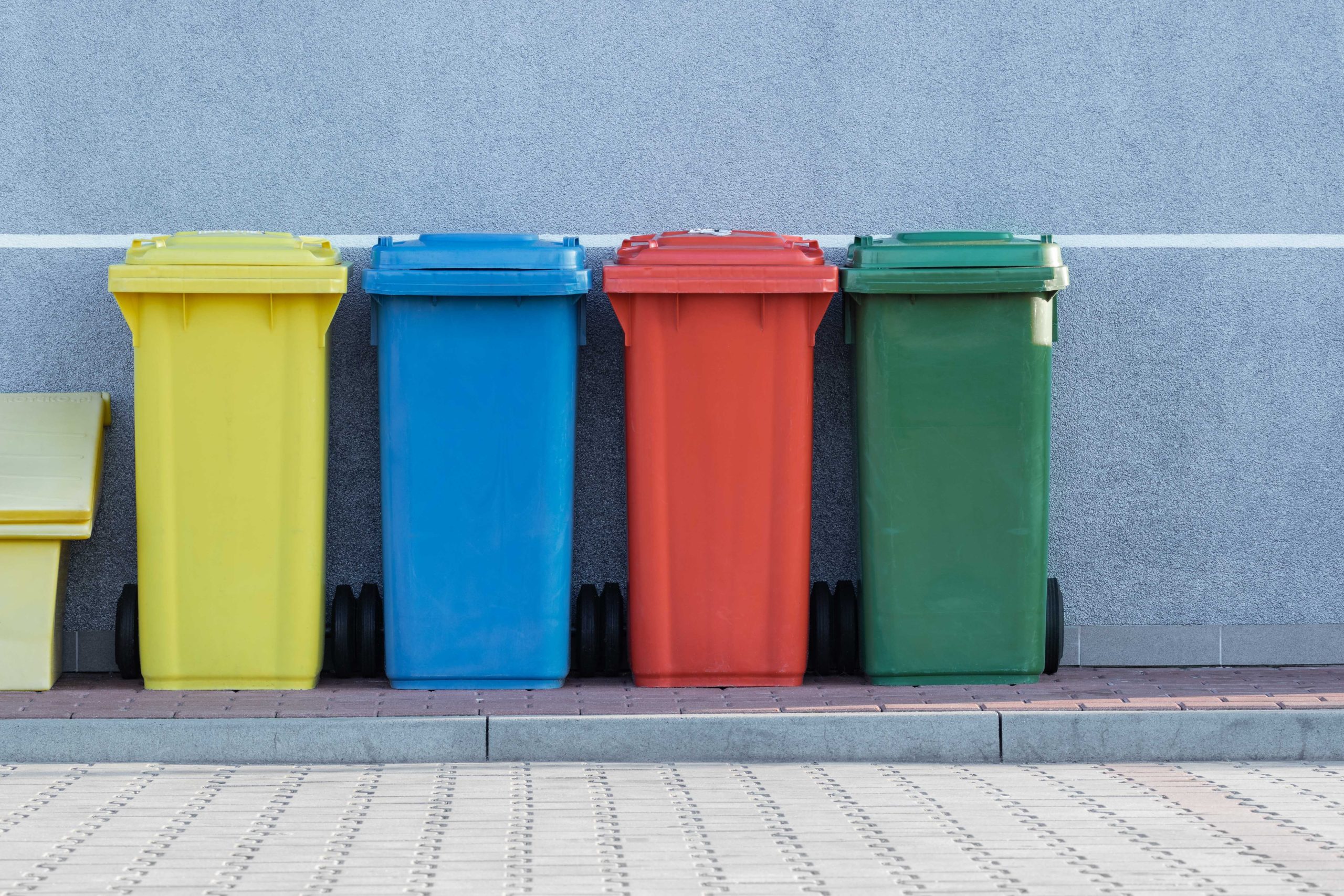 A row of colorful trash cans next to a wall, showcasing waste management principles.