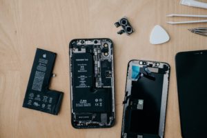 A broken iPhone, a form of waste from electrical and electronic equipment, is sitting on a wooden table.